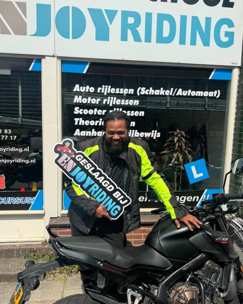 Geslaagde cursist Clayd met motorrijbewijs en congratulatiebord bij rijschool EnjoyRiding Geslaagde cursist Clayd met motorrijbewijs en congratulatiebord bij rijschool EnjoyRiding