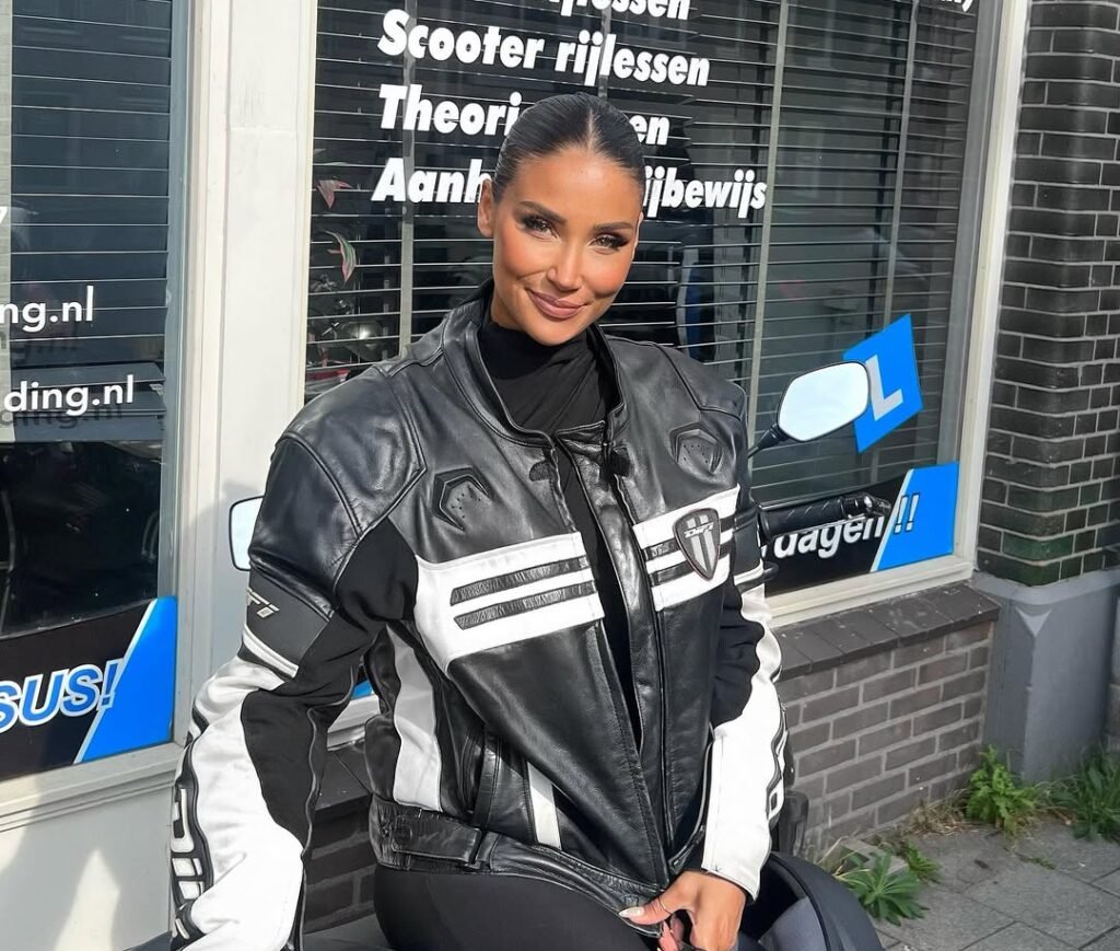 Geslaagde cursiste in motorkleding poseert trots voor rijschool na het behalen van haar motorrijbewijs Geslaagde cursiste in motorkleding poseert trots voor rijschool na het behalen van haar motorrijbewijs
