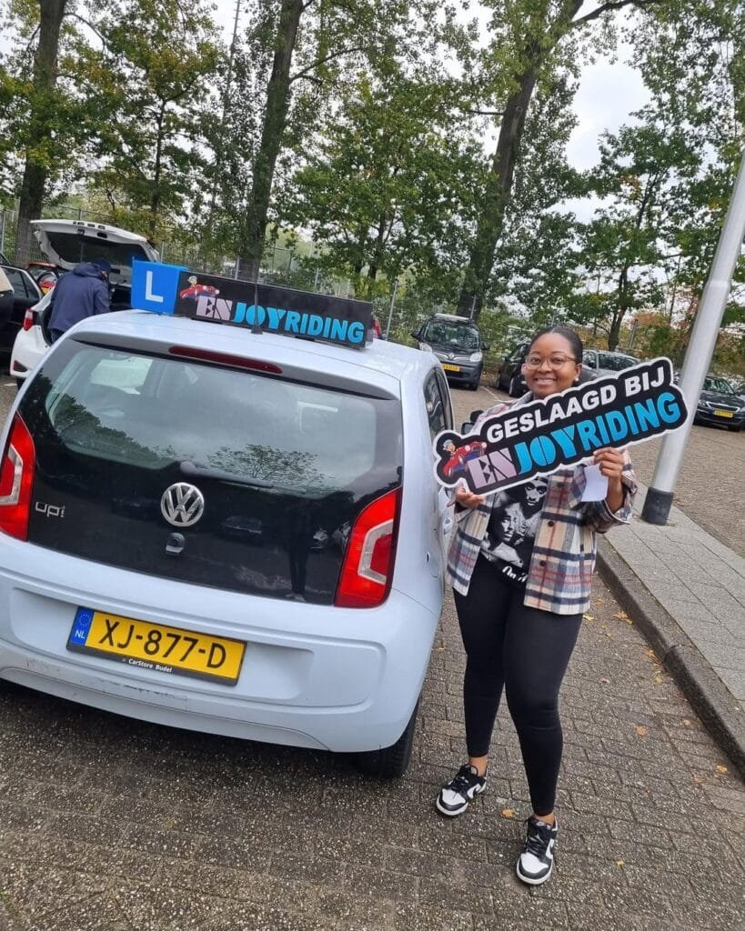Geslaagde leerling toont trots haar rijbewijs certificaat naast Volkswagen lesauto van rijschool EnjoyRiding Geslaagde leerling toont trots haar rijbewijs certificaat naast Volkswagen lesauto van rijschool EnjoyRiding