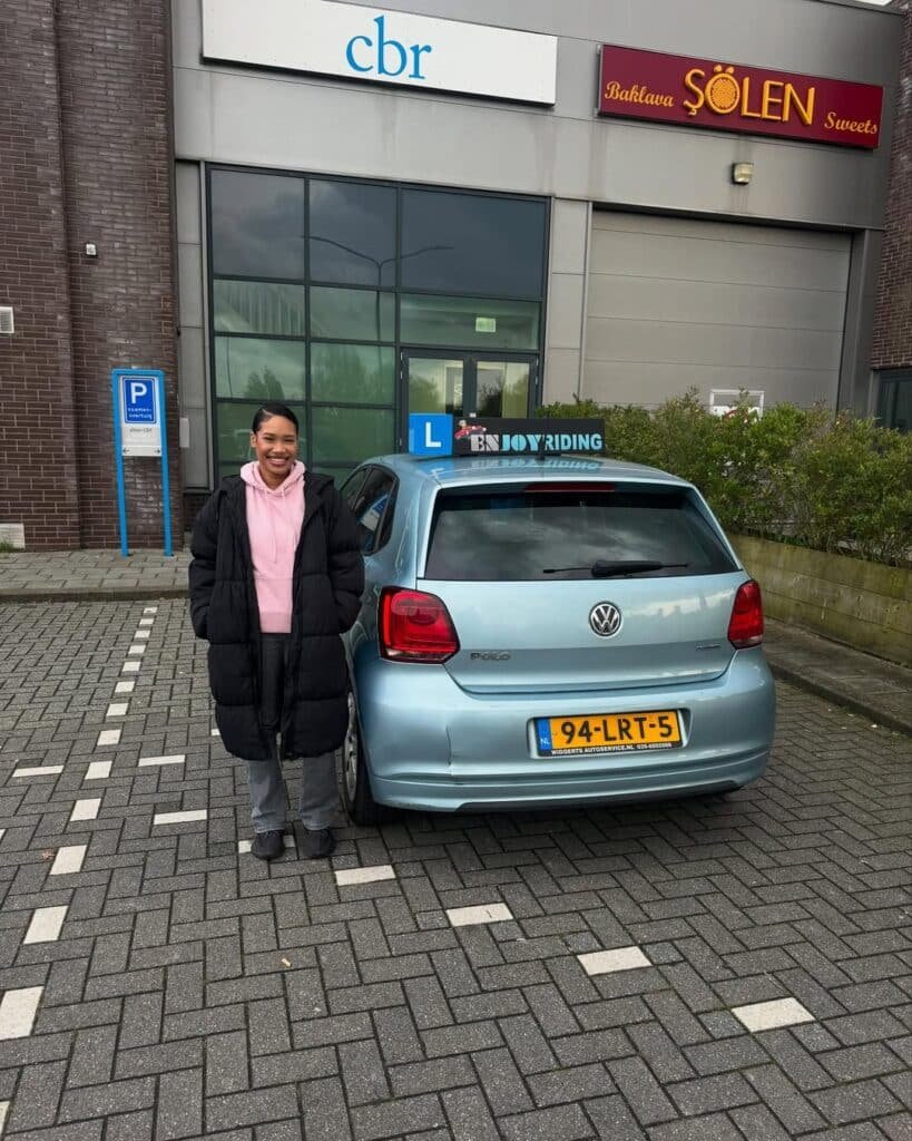 Geslaagde leerling van Rijschool EnjoyRiding poseert trots naast lesauto na het behalen van rijbewijs Geslaagde leerling van Rijschool EnjoyRiding poseert trots naast lesauto na het behalen van rijbewijs
