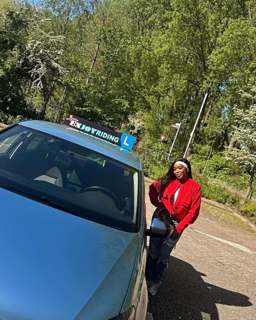 Geslaagde leerling van rijschool EnjoyRiding poseert trots bij lesauto met L-teken na rijexamen Geslaagde leerling van rijschool EnjoyRiding poseert trots bij lesauto met L-teken na rijexamen