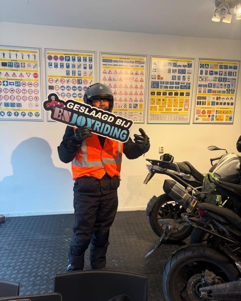 Geslaagde motorrijder met diploma van rijschool EnjoyRiding in klaslokaal met verkeersborden Geslaagde motorrijder met diploma van rijschool EnjoyRiding in klaslokaal met verkeersborden